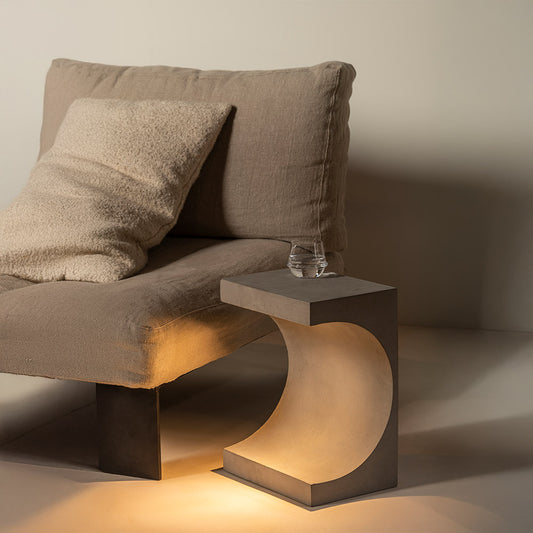 diffuse licht van de betonnen bijzettafel 'Tangent' bij een fauteuil