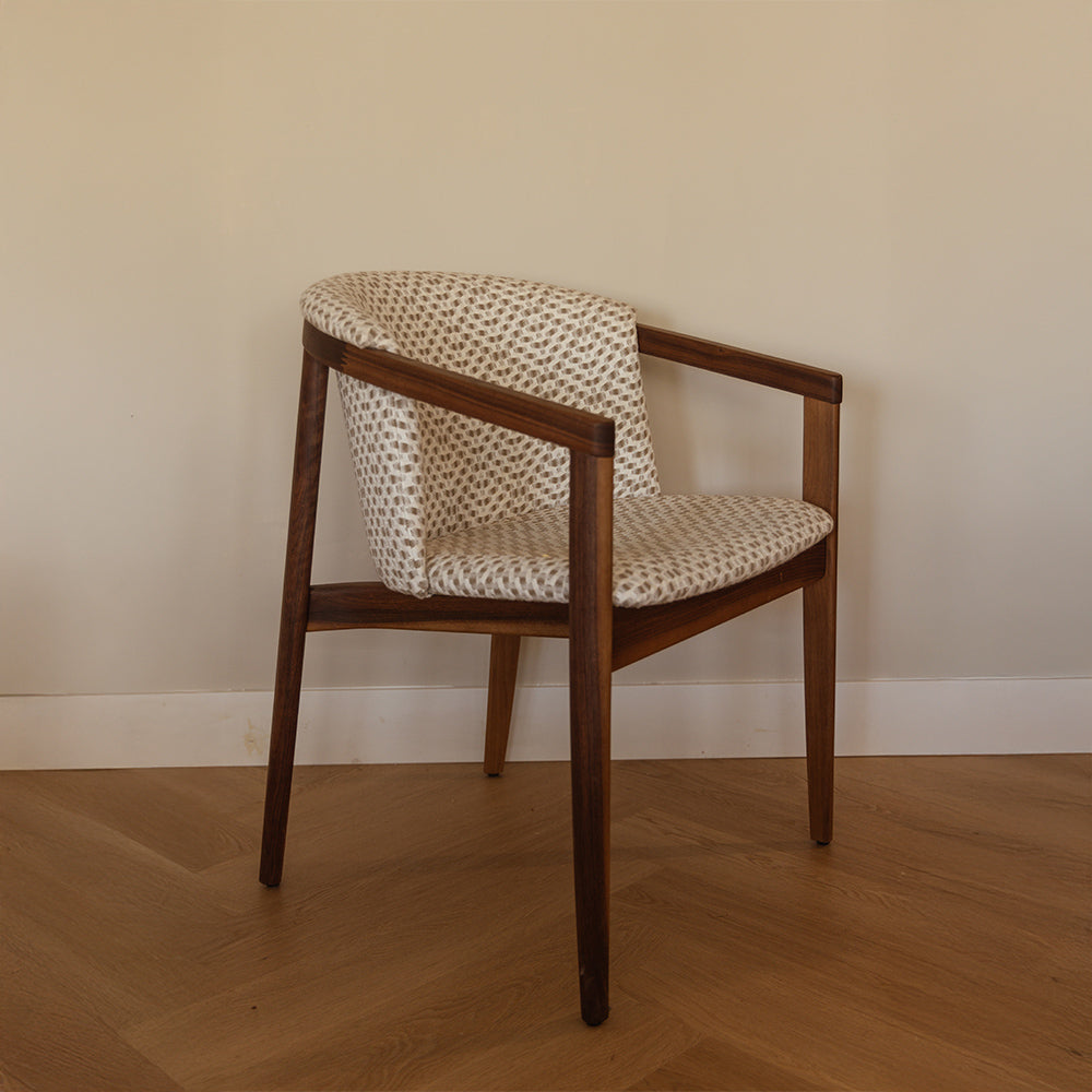 moderne rose stoel van notenhout en stof met armleuning voor een witte muur.